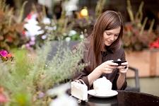 The image includes a woman sitting in a Cafe, having her phone in the hands