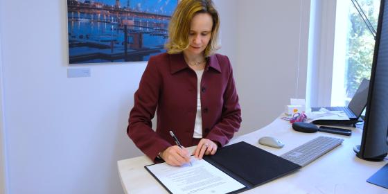 The image shows the Director of the BEREC Office, Verena Weber, signing the Green Charter.