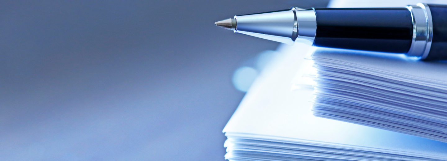 The image shows a pile of documents with a pen laying on top of them